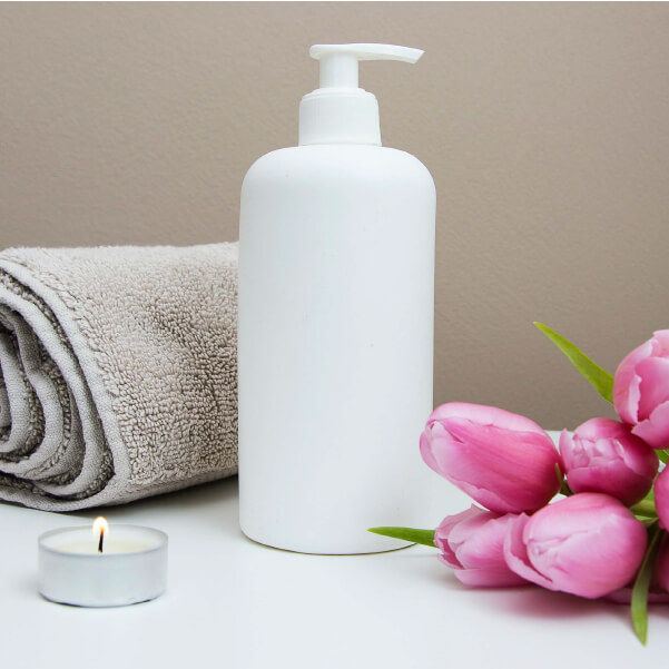 Image of lotion with a candle and tan towel to the left, and pink tulips to the right