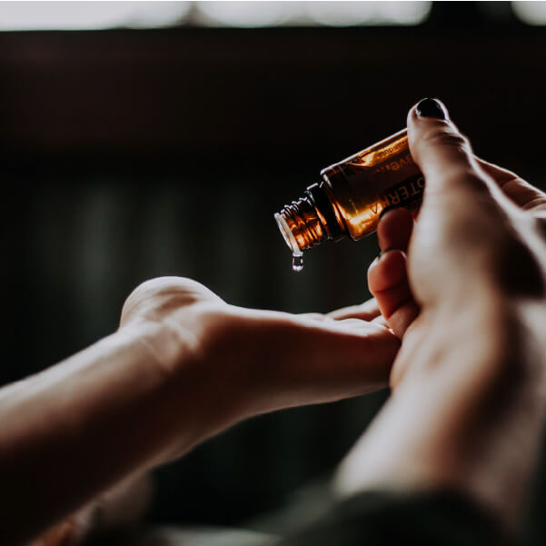 Closeup image of hands, one hand with palm facing up, another hand, tilting a bottle of essential oils onto the open palm