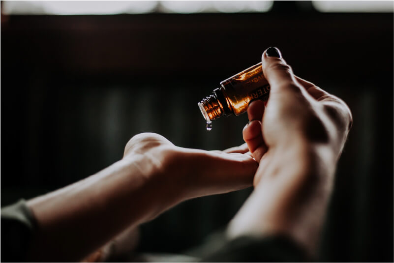 Closeup image of hands, one hand with palm facing up, another hand, tilting a bottle of essential oils onto the open palm